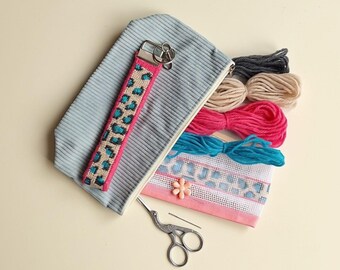 Peut inclure: Une pochette zippée en velours côtelé bleu clair avec une dragonne à motif léopard, accompagnée de quatre écheveaux de laine gris, beige, rose et bleu sarcelle, un morceau de toile avec un bouton fleur et une paire de ciseaux à broder en métal argenté.