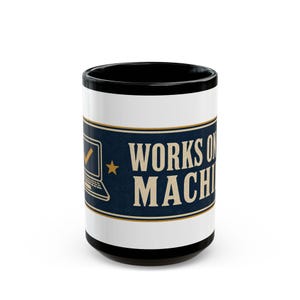 May include: A white ceramic mug with a black interior and rim, featuring a dark blue horizontal band with gold trim. The design includes a gold laptop icon with a checkmark, a gold star, and the text "WORKS ON MY MACHINE" in bold gold lettering.