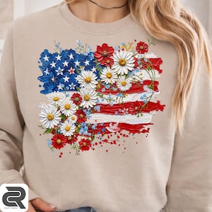 Könnte beinhalten: Ein beigefarbenes Sweatshirt mit Rundhalsausschnitt und einem Grafikdruck der amerikanischen Flagge in strukturierter Impasto-Optik. Die Flagge ist mit Gruppen aus weißen Gänseblümchen, roten Mohnblumen und kleinen blauen Blüten verziert.