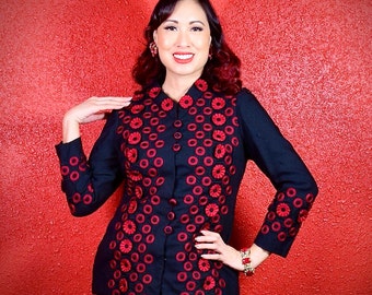 May include: A black blazer with red embroidered circles. The blazer has a mandarin collar and long sleeves.