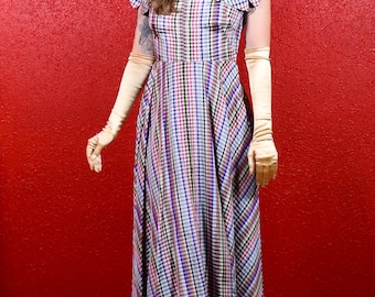 May include: A woman wearing a long, plaid dress with a white collar and short sleeves. She is wearing long, white gloves and has her hair pulled back.