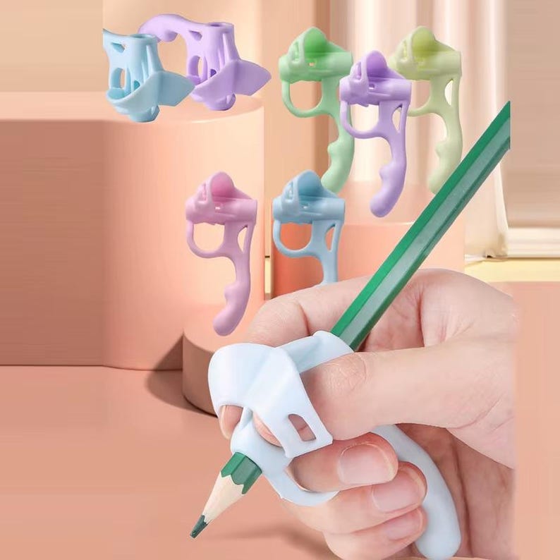 May include: A collection of ergonomic pencil grips in pastel shades of light blue, lavender, and mint green. Each grip features a contoured shape with finger slots designed to fit onto a standard pencil, shown here in white on a green pencil.