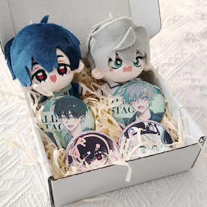 Könnte beinhalten: Eine weiße Pappschachtel gefüllt mit Papierstreifen, die zwei Plüschpuppen mit blauem und silbernem Haar sowie vier runde Ansteckbuttons mit Anime-Charakterillustrationen und dem Text ALL STAGE enthält.