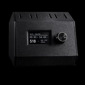Peut inclure: Appareil électronique noir avec un petit écran affichant des chiffres et du texte, dont "518". Il possède un bouton sur le côté droit et une surface texturée. L'appareil est posé sur un fond noir.