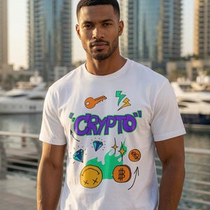 Puede incluir: Una camiseta blanca de manga corta con un estampado gráfico colorido que incluye la palabra CRYPTO en letras moradas, una llave naranja, rayos amarillos, diamantes azules, una cara sonriente amarilla con ojos en X y monedas naranjas.