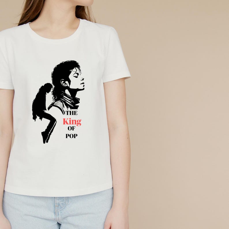 May include: A white short-sleeved t-shirt featuring a black graphic of a person in profile and a silhouette of a person dancing. The text "THE" and "OF POP" are printed in black, while the word "King" is printed in red below the profile.