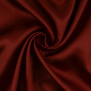 May include: A deep burgundy fabric with a smooth, lustrous surface texture. The material is gathered into a central swirl, creating soft, flowing folds and shadows that highlight the rich, dark red color and the reflective quality of the textile.