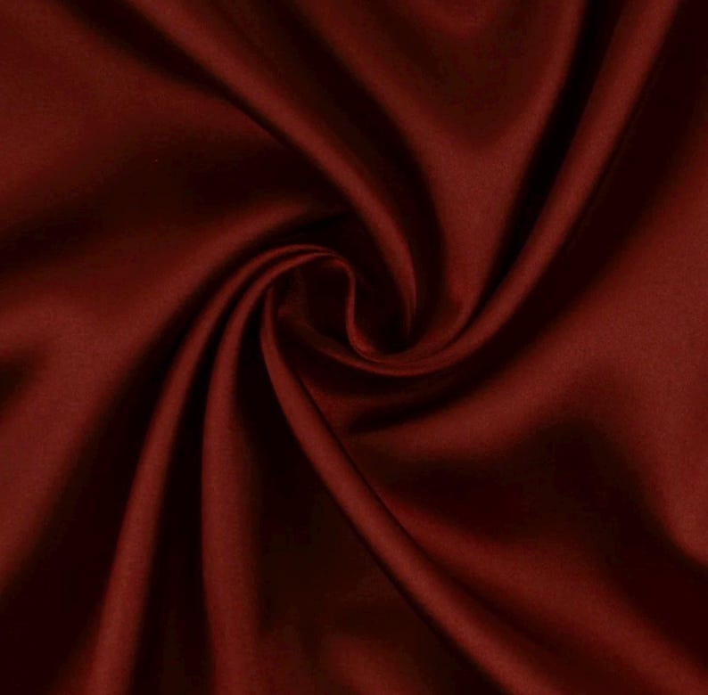 May include: A deep burgundy fabric with a smooth, lustrous surface texture. The material is gathered into a central swirl, creating soft, flowing folds and shadows that highlight the rich, dark red color and the reflective quality of the textile.