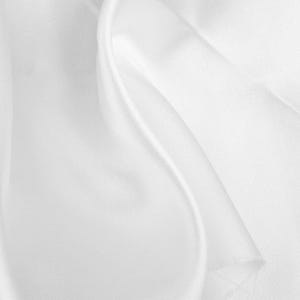 May include: A piece of solid white fabric with a smooth, lustrous surface and a soft sheen. The material is draped in gentle, flowing folds that create subtle highlights and shadows, emphasizing the fine texture and consistent bright white color.