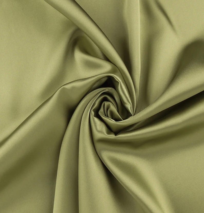 May include: A solid olive green fabric with a smooth, lustrous finish. The material is gathered in the center, creating deep, flowing folds and soft shadows that highlight the reflective quality and uniform texture of the textile surface.