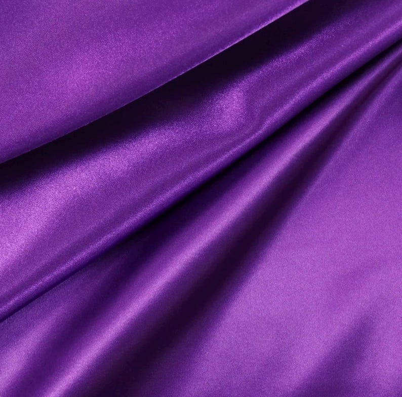 May include: A vibrant purple fabric with a smooth, lustrous finish and a reflective surface. The material is draped in soft, flowing folds that create deep shadows and bright highlights, emphasizing the silky texture and rich, saturated color.