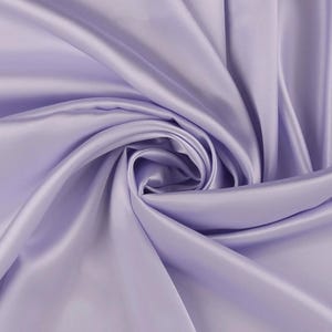 May include: A solid light lavender fabric with a smooth, lustrous finish. The material is draped in a central spiral pattern, creating deep, flowing folds and soft shadows that highlight the reflective, silky texture of the textile surface.
