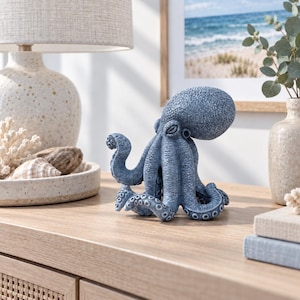 May include: A blue octopus figurine with a textured, bumpy surface and visible suckers on its tentacles. The sculpture is depicted in a standing position with its tentacles curled at the base, showcasing a detailed, realistic marine animal design.