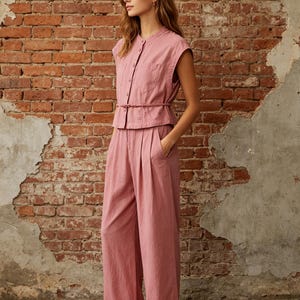 May include: A dusty rose two-piece set consisting of a sleeveless button-down top with a mandarin collar and a chest pocket, paired with matching high-waisted wide-leg trousers featuring front pleats and a thin tie belt at the waist.