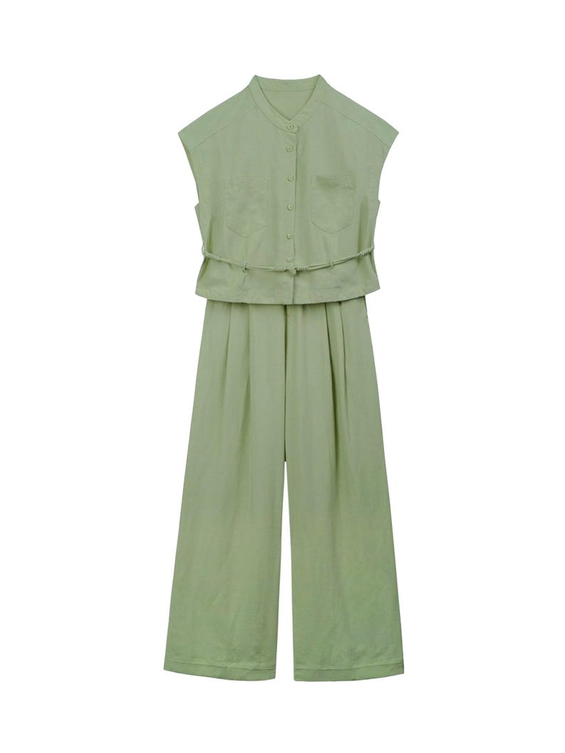 May include: A light sage green sleeveless jumpsuit featuring a mandarin collar, a button-down front closure, two chest pockets, and a thin matching fabric belt at the waist. The garment has wide-leg trousers with subtle pleats at the front.