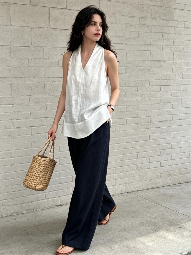 May include: A sleeveless white V-neck top paired with loose-fitting black wide-leg trousers. The outfit is accessorized with a woven straw bucket bag and brown leather thong sandals, creating a simple and functional ensemble for warm weather.