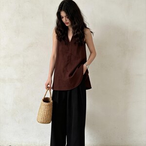 May include: A dark brown sleeveless top with a V-neckline paired with loose-fitting black wide-leg trousers. The outfit is accessorized with a small woven straw handbag and dark brown closed-toe shoes, creating a simple and cohesive ensemble.