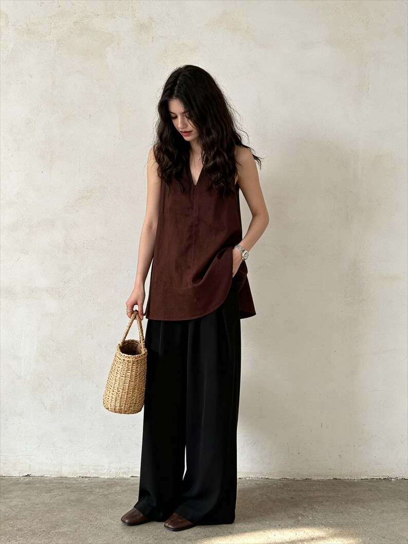 May include: A dark brown sleeveless top with a V-neckline paired with loose-fitting black wide-leg trousers. The outfit is accessorized with a small woven straw handbag and dark brown closed-toe shoes, creating a simple and cohesive ensemble.