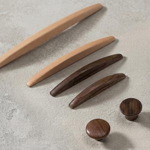 May include: A collection of six wooden cabinet hardware pieces including two long light-toned wooden pulls, two medium-length dark-toned wooden pulls, and two small round dark-toned wooden knobs, all featuring a smooth, natural wood grain finish.