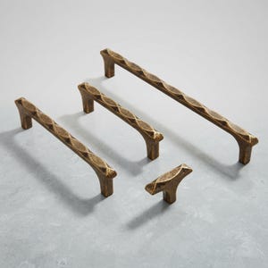 Op de afbeelding: Een set van vier kastbeslagstukken in een donkere antieke messing afwerking. De set bevat drie langwerpige ladehandgrepen en één knop met enkel gat, allemaal voorzien van een herhalend ruitvormig textuurpatroon op het bovenoppervlak.