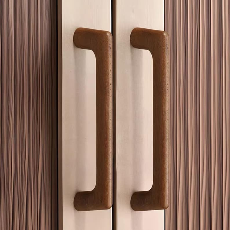 May include: Two vertical door handles made of dark brown wood with a smooth, rounded finish. The handles are mounted on a light-coloured, metallic-looking door panel that features a subtle, vertical, wavy texture across the entire surface area.