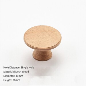 May include: A round light brown beech wood cabinet knob with a flat circular top and a tapered base. The knob features a single hole mounting design, a diameter of 40mm, and a height of 26mm. The wood grain is visible across the surface.