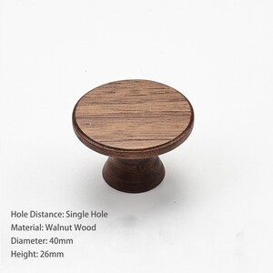 May include: A round walnut wood cabinet knob with a single hole mounting design. The knob features a flat circular top and a tapered base. The dimensions are 40mm in diameter and 26mm in height, as specified by the text in the image.