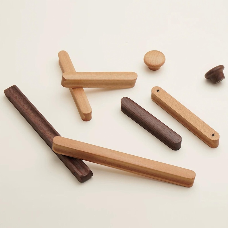 May include: A collection of wooden cabinet hardware including several long rectangular drawer pulls and two round knobs. The hardware is crafted from light-toned and dark-toned wood, featuring smooth, rounded edges and visible screw holes.
