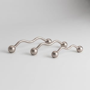 May include: Three matte silver cabinet pulls arranged in a row, each featuring a wavy, serpentine metal bar design with a spherical knob at both ends. The hardware has a smooth, uniform metallic finish and a curved, undulating shape throughout.