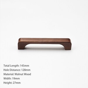 May include: A dark brown walnut wood cabinet handle with a curved underside. The handle has a total length of 145mm, a hole distance of 128mm, a width of 19mm, and a height of 27mm. The text on the image specifies these exact dimensions.