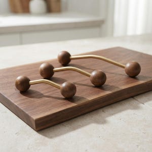 May include: Three cabinet pulls arranged in a row, each featuring a curved gold-toned metal bar connected to two smooth, spherical dark brown wooden knobs at either end. The pulls vary in length, showcasing a consistent design of metal and wood.
