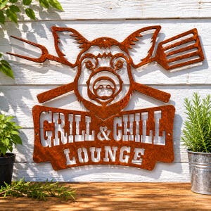 Könnte beinhalten: Ein rostfarbenes Metall-Wandschild mit der Silhouette eines Schweinekopfes zwischen einer Grillgabel und einem Pfannenwender. Unter dem Schwein befindet sich ein rechteckiges Banner mit dem ausgeschnittenen Text "GRILL & CHILL LOUNGE".