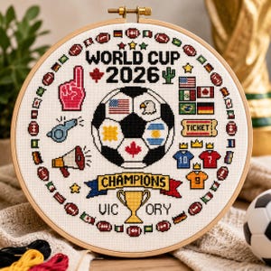 May include: A circular wooden embroidery hoop containing a cross-stitch design featuring a soccer ball, the text WORLD CUP 2026, CHAMPIONS, and VICTORY, surrounded by small flags, sports icons, and jerseys on a white fabric background.
