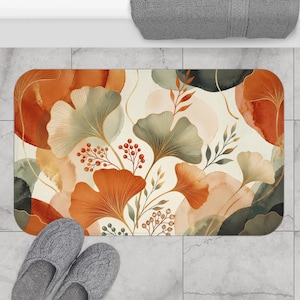 May include: A rectangular bath mat featuring a watercolour-style botanical print with ginkgo leaves and berry sprigs in shades of burnt orange, sage green, and cream. The design includes overlapping abstract shapes and fine gold-toned line details.