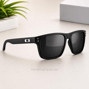 May include: Black sunglasses featuring a rectangular frame with dark tinted lenses. The temples display a silver rectangular logo emblem near the hinges, complemented by two small silver metallic studs on the front corners of the frame.