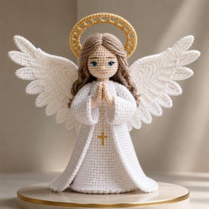 May include: A handcrafted crochet angel figurine with white wings, a halo, and a white dress. The angel has brown hair, blue eyes, and clasped hands. A gold cross hangs from the angel's hands. The figurine is displayed on a round, gold-trimmed base.