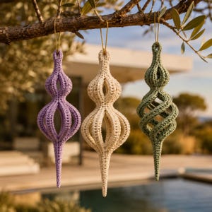 May include: Three hanging ornaments crafted from crocheted yarn in lavender, cream, and sage green. Each ornament features a hollow, elongated, spiraling structure with a pointed bottom and a thin gold string loop attached to the top for hanging.