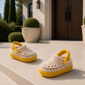 Könnte beinhalten: Ein Paar handgehäkelte Clogs mit einem cremefarbenen Obermaterial mit Lochmuster und einer einfarbigen gelben Sohle. Jeder Schuh verfügt über einen passenden gelben Fersenriemen, der mit einem runden gelben Knopf an der Seite befestigt ist.