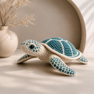 Pode incluir: Uma tartaruga marinha de crochê em creme e azul-petróleo. A tartaruga tem uma carapaça azul-petróleo com detalhes brancos, corpo creme e barbatanas azul-petróleo. Está sobre uma superfície clara.