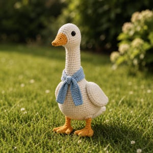 Puede incluir: Un ganso de ganchillo hecho a mano con cuerpo color crema, pico y patas naranjas y una bufanda azul. El ganso tiene ojos negros y está sobre hierba verde. Un artículo decorativo encantador y caprichoso.