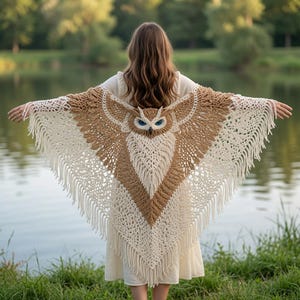 May include: A triangular crochet shawl featuring a detailed owl design with prominent blue eyes, rendered in shades of tan and cream yarn. The shawl has an intricate openwork pattern and is finished with long, dangling fringe along the bottom edges.
