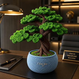 May include: A crocheted bonsai tree with a brown twisted trunk and vibrant green foliage, potted in a light blue crocheted container. The container features the embroidered text "I Love You" with a small heart symbol centered on the front.