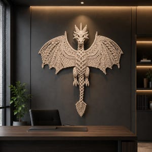 May include: A large, intricate macramé wall hanging shaped like a dragon with expansive, detailed wings and a long, textured tail. The piece is crafted from light beige cord, featuring complex knot patterns throughout the body and wings.