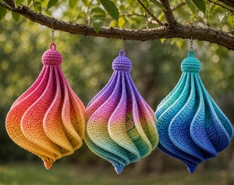 May include: Three hanging crochet ornaments with a spiral, teardrop-shaped design. The left ornament features a pink to orange gradient, the centre displays a rainbow spectrum, and the right ornament shows a teal to deep blue colour transition.