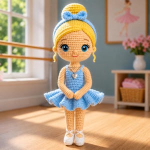 Puede incluir: Muñeca de bailarina de ganchillo hecha a mano con cabello rubio recogido en un moño y un lazo azul. La muñeca lleva un tutú azul, un colgante en forma de corazón y zapatillas de ballet blancas. La muñeca está en una habitación con una barra de ballet y una imagen enmarcada.
