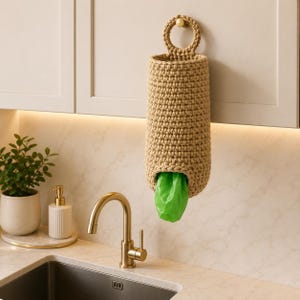 May include: A cylindrical beige crochet bag with a circular top handle hanging from a cabinet knob. The bag features a bottom opening with a bright green plastic bag protruding from the center, showcasing a textured, hand-stitched yarn construction.