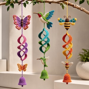 May include: Three hanging crochet ornaments suspended from a branch. The first features a purple butterfly, a spiral, an orange butterfly, and a purple bell. The second has a hummingbird, a green spiral, a smaller hummingbird, and a green bell. The third has a bee, an orange spiral, a smaller bee, and an orange bell.
