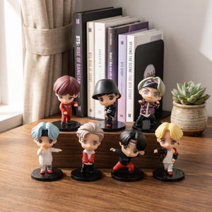 May include: Seven miniature chibi-style figurines of young people with diverse hair colours and outfits, each standing on a circular black base. The figures are arranged in two rows in front of a collection of books titled BTS: Rise of Bangtan.
