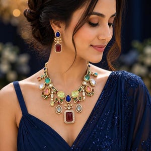 May include: A necklace and matching drop earrings featuring multi-colored gemstones in various shapes, including rectangular, oval, and teardrop cuts. The jewelry set is crafted with gold-toned metal settings and small white accents surrounding the stones.