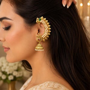 Può includere: Un set di ear cuff e orecchino jhumka color oro con motivo a pavone, una pietra verde sulla parte superiore, una pietra rossa al centro e dettagli in filigrana. Il gioiello è decorato con piccole perle bianche lungo il bordo e la base.